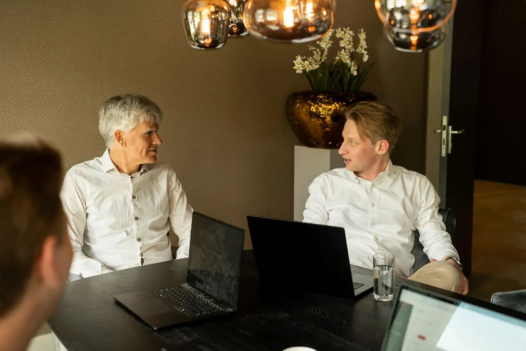 Twee collega's in gesprek aan de vergadertafel met laptops