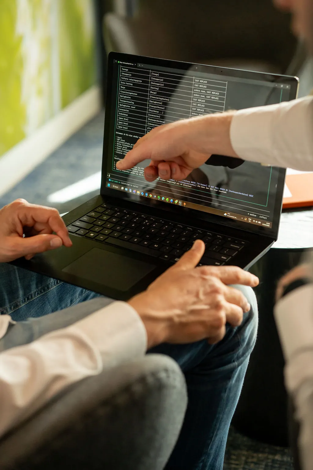 Handen op een laptop met SQL-code, uitleg aan een collega