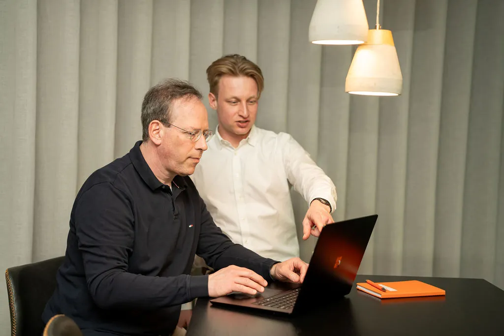 Twee ITsmart-collega's samen achter een laptop met oranje notitieboek