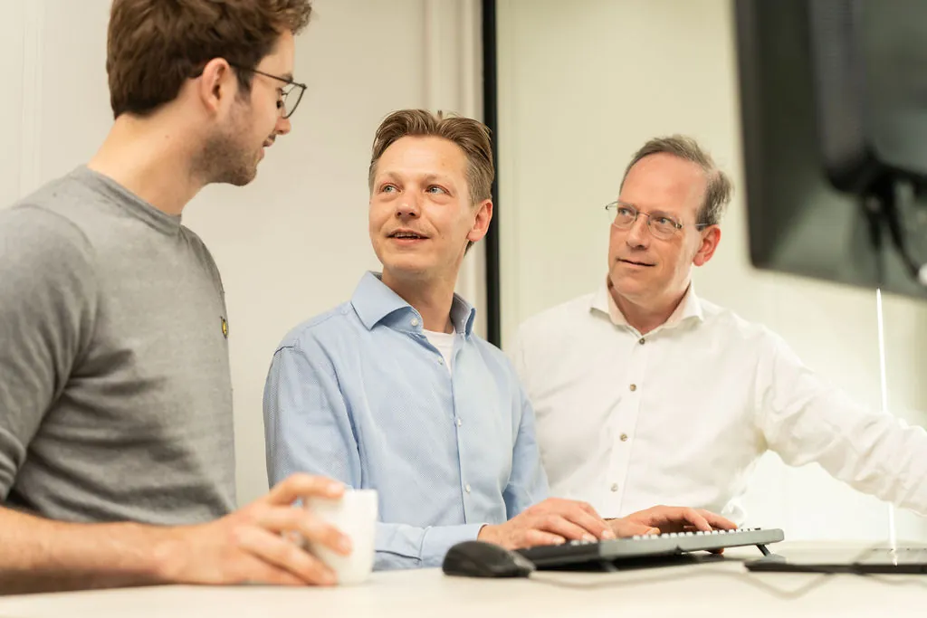Drie collega's kijken geconcentreerd naar een monitor met een code-editor