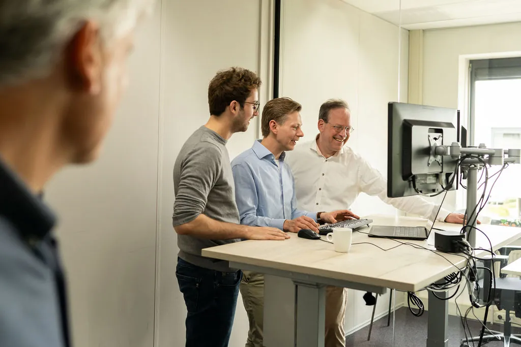 Drie collega's van ITsmart lachend met koffie bij een monitor