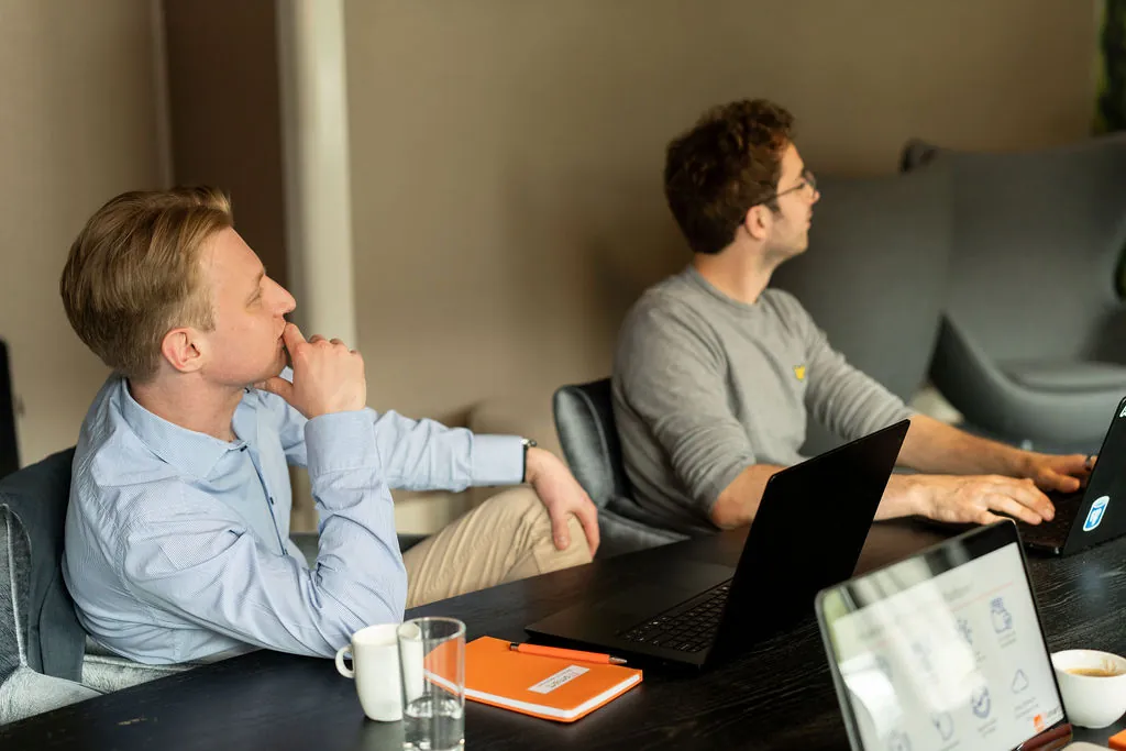 Twee toehoorders met laptops en een oranje ITsmart-notitieboek in de vergaderzaal